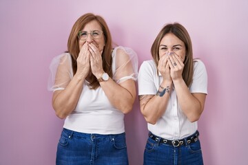 Hispanic mother and daughter wearing casual white t shirt over pink background laughing and...