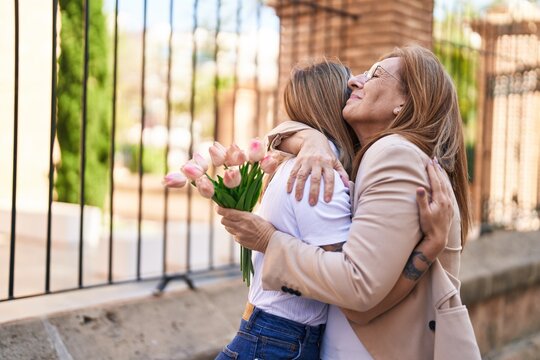 Mother and daughter hugging each other holding bouquet of flowers at street