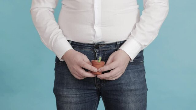 A man holds a small pot of cactus in front of his groin. Small penis concept, male penis enlargement surgery, close-up