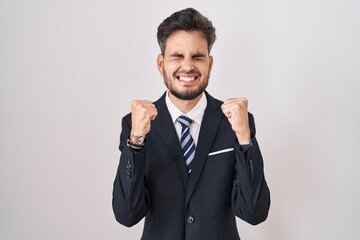 Young hispanic man with tattoos wearing business suit and tie excited for success with arms raised and eyes closed celebrating victory smiling. winner concept.