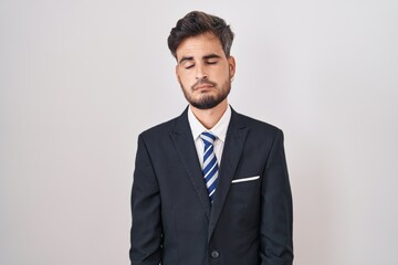 Young hispanic man with tattoos wearing business suit and tie looking sleepy and tired, exhausted for fatigue and hangover, lazy eyes in the morning.
