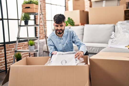 Young hispanic man unpacking cardboard box at new home