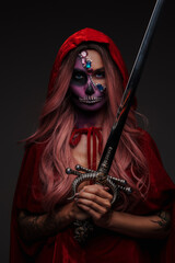 Shot of stylish witch with muertos makeup dressed in red cape and holding sword.
