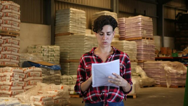 Latin woman making stock control, verifying documents while working warehouse.