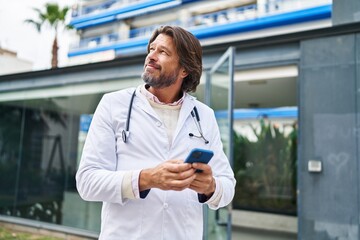 Middle age man doctor smiling confident using smartphone at hospital