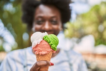 Young african woman smiling eating ice cream at park