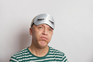 tired man in a sleep mask on a gray background, insomnia of the elderly concept, sleep problems