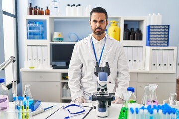 Young hispanic man with beard working at scientist laboratory skeptic and nervous, frowning upset because of problem. negative person.