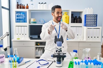 Fototapeta premium Young hispanic man with beard working at scientist laboratory pointing fingers to camera with happy and funny face. good energy and vibes.
