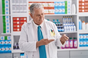Middle age grey-haired man pharmacist holding glasses at pharmacy