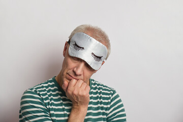 tired man in a sleep mask on a gray background, insomnia of the elderly concept, sleep problems