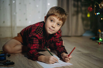  portrait of preschooler boy in plaid shirt laying on the floor writing christmas letter to santa
