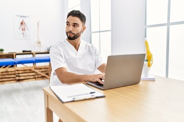 Young arab man wearing physiotherapist uniform using laptop at clinic