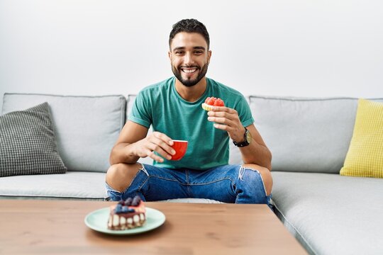 Young arab man having breakfast sitting on sofa at home