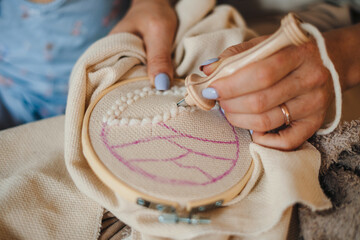 Close-up portrait of a female sitting on the floor with thread and needle, girl embroidering,...