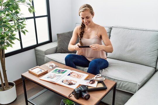 Young caucasian woman making picture to photo book sitting on sofa at home