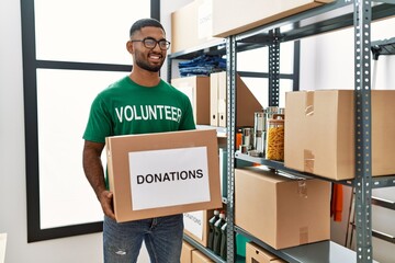 Young arab man wearing volunteer uniform holding donations box at charity center
