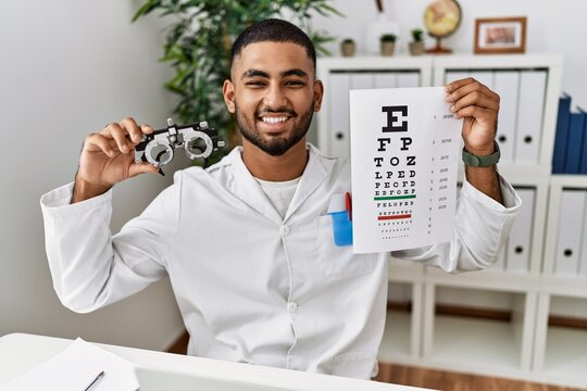 Young arab man holding sneller test and optometry glasses at clinic