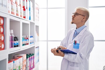 Young caucasian man pharmacist writing on document at pharmacy