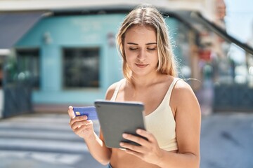 Young blonde woman using touchpad and credit card at street