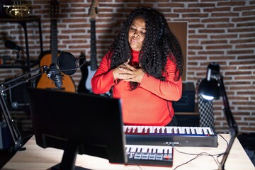 Plus size hispanic woman playing piano at music studio smiling with hands on chest with closed eyes and grateful gesture on face. health concept.