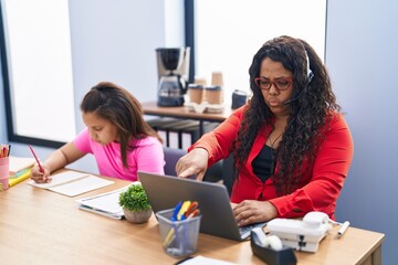 Mother and young daughter at the office working and doing homework pointing with finger to the...