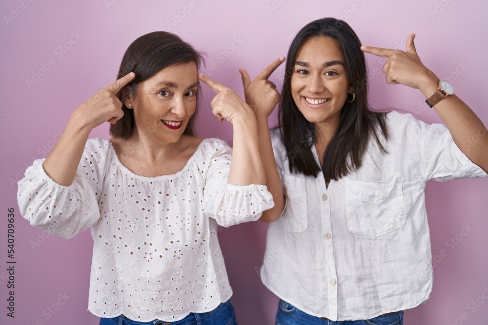 Poster Hispanic mother and daughter together smiling pointing to head with both hands finger, great idea or thought, good memory