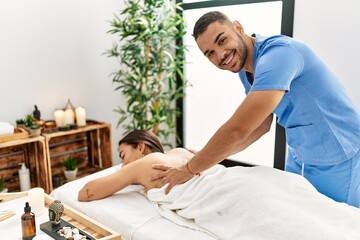 Obraz premium Latin man and woman wearing physiotherapy uniform having rehab session massaging back at beauty center