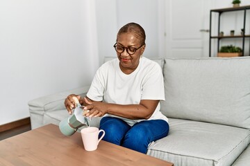 Senior african american woman smiling confident pouring coffee on cup at home