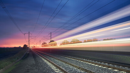 Obraz na płótnie Canvas Modern railway at beautiful sunrise. Light trail of high speed train on railroad track. Moving modern intercity passenger train..