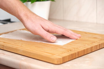 A man wipes a bamboo cutting board with a white paper napkin after washing with water. Careful handling of wood products. Bamboo cutting board. Treatment with mineral oil. Drying of the cutting board. - obrazy, fototapety, plakaty