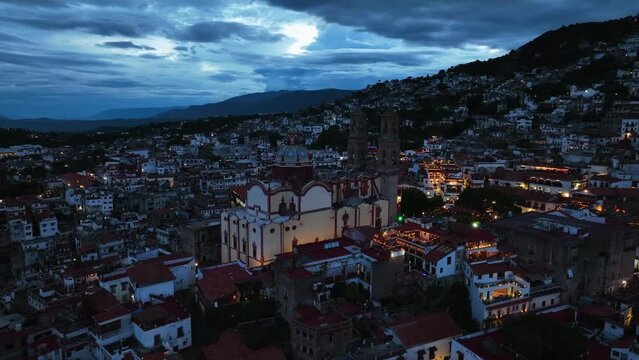 Aerial view away from the church of Santa prisca de Taxco, gloomy evening in Mexico - rotating, pull back, drone shot