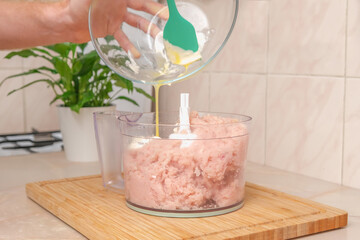 A man adds an egg with mayonnaise to food processor with chopped chicken meat. A food processor with pieces of chicken breast with mayonnaise and egg. The process of cooking chopped chicken cutlets.