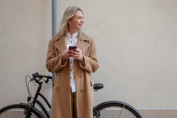 Blonde woman in a beige coat with a bike in the street
