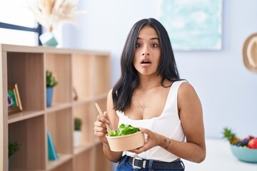 Brunette woman eating a salad at home afraid and shocked with surprise and amazed expression, fear and excited face.