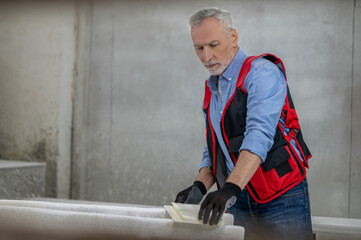 Craft man in red vest with a piece of wood for painting