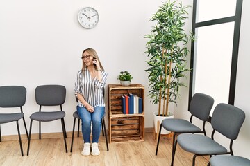 Young chinese woman talking on the smartphone sitting on chair at waiting room