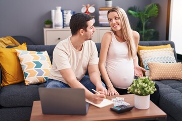 Man and woman couple expecting baby writing on notebook accounting at home