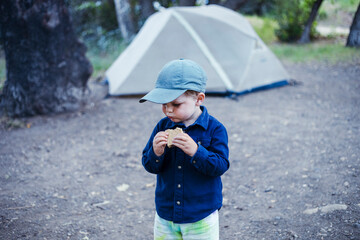 Cute boy wearing cap eating smore in front of tent