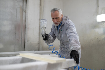 Mature man in protective clothing painting wood with a spray gun