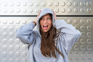 Woman with mouth open wearing hooded shirt in front of metal wall