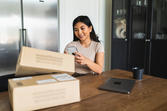 Smiling woman checking home delivery box at dining table
