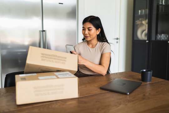 Young woman taking picture of delivery package box at dining table