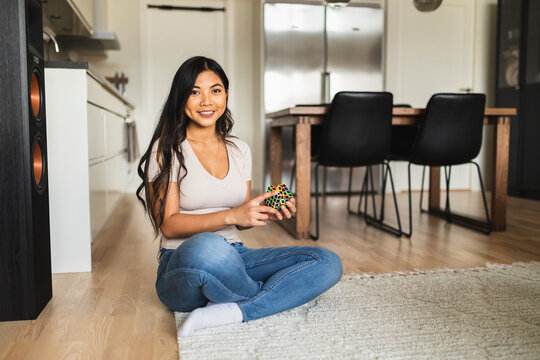 Happy woman with puzzle cube sitting on carpet at home