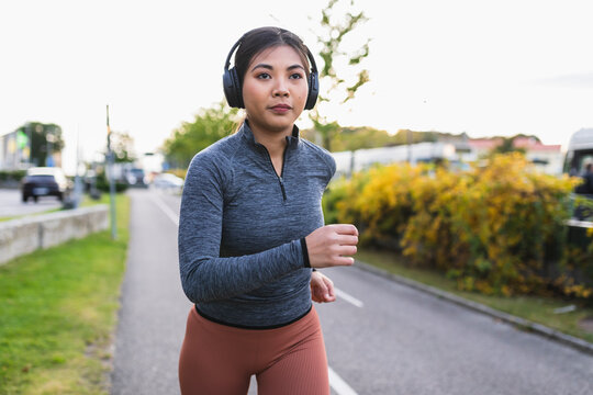 Young woman listening to music and jogging on road