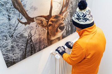 Senior man wearing warm clothing in front of radiator at home