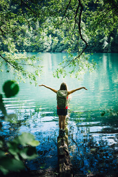 Woman with arms outstretched standing on tree log at Lake Levico