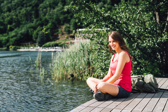 Happy hiker sitting cross-legged on jetty by Lake Levico