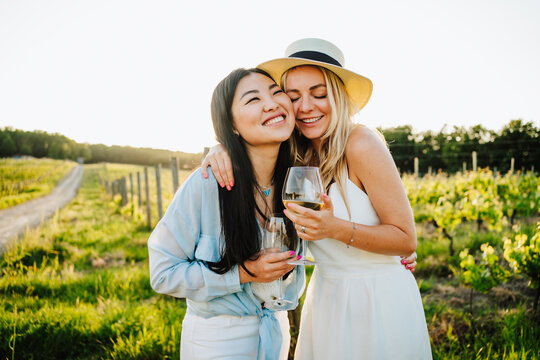 Happy friends holding glass of wine embracing at winery