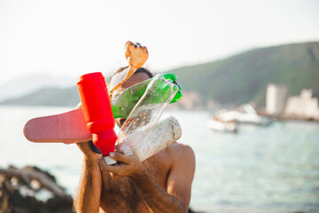 Young man holding empty plastic bottles and slipper in front of face